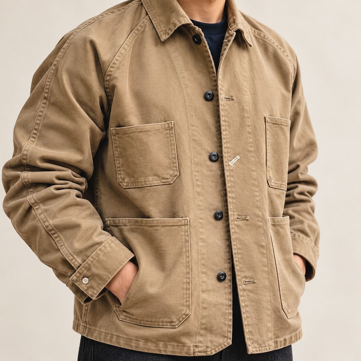 Close front view of the khaki chore coat worn over a navy shirt, showing four patch pockets and a button front