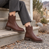 Briarwalk dark-brown ankle boots worn while seated on a neighborhood porch step