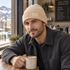 Man holding a coffee mug at a local coffee shop wearing the WRELS beige ribbed beanie