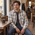 Man seated inside an independent coffee shop wearing the Ridgepine gray and taupe plaid shirt