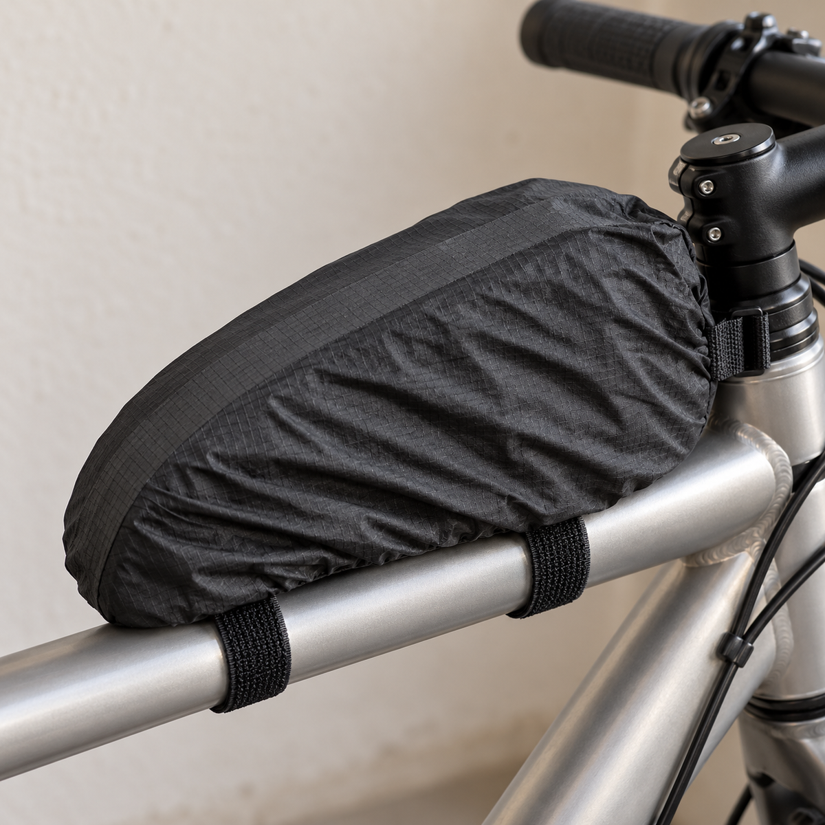 Black rain cover deployed over a Topeak TopLoader bag mounted on a silver bicycle top tube