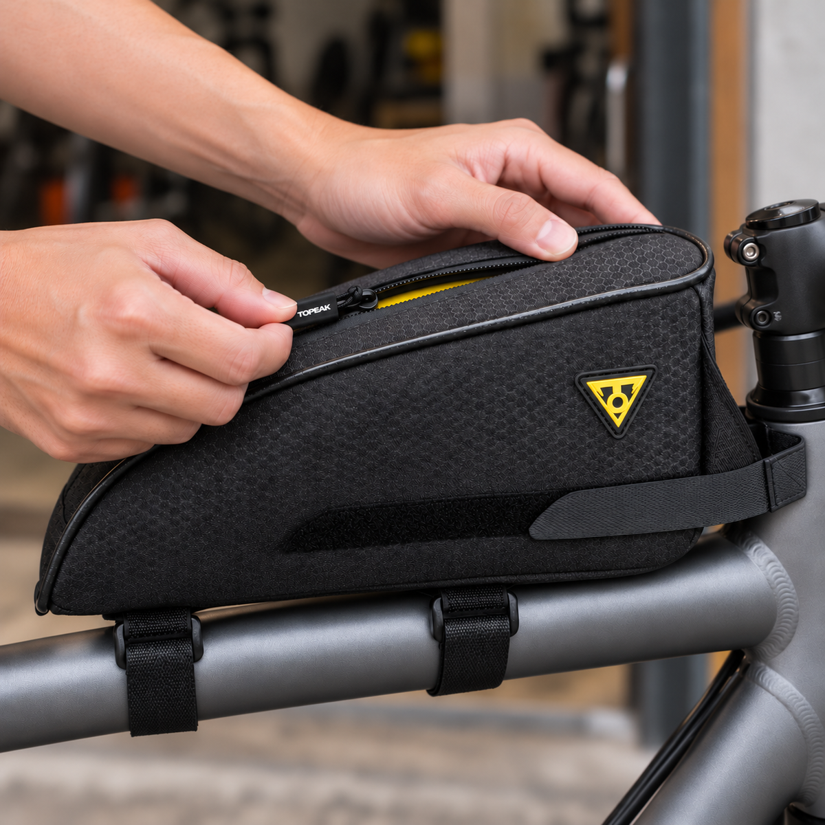 Hands partially opening the zipper of a black Topeak TopLoader bag, revealing a narrow strip of yellow lining