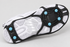 Underside of a black Due North Everyday G3 traction aid on a white athletic shoe, showing four forefoot spikes and two heel spikes.