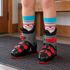 White and turquoise patterned Bridgedale kids ski socks worn above the padded cuffs of two junior ski boots on an entry mat.