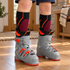 Black Fox River Boreal kids ski socks with orange and magenta calf details visible above grey ski-boot liners, worn on a wooden floor.