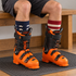 Fox River Old Glory complementary star-and-stripe sock cuffs visible above two orange-and-black illustrative ski boots on a rubber mat.
