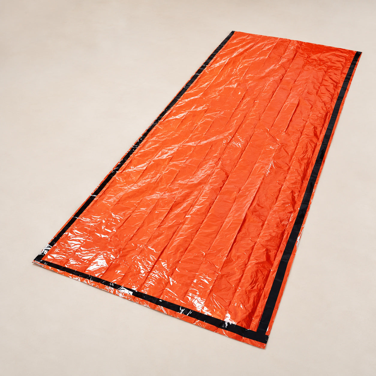 Orange thin-film bivy cover laid flat with black edging and a small silver-colored reverse edge