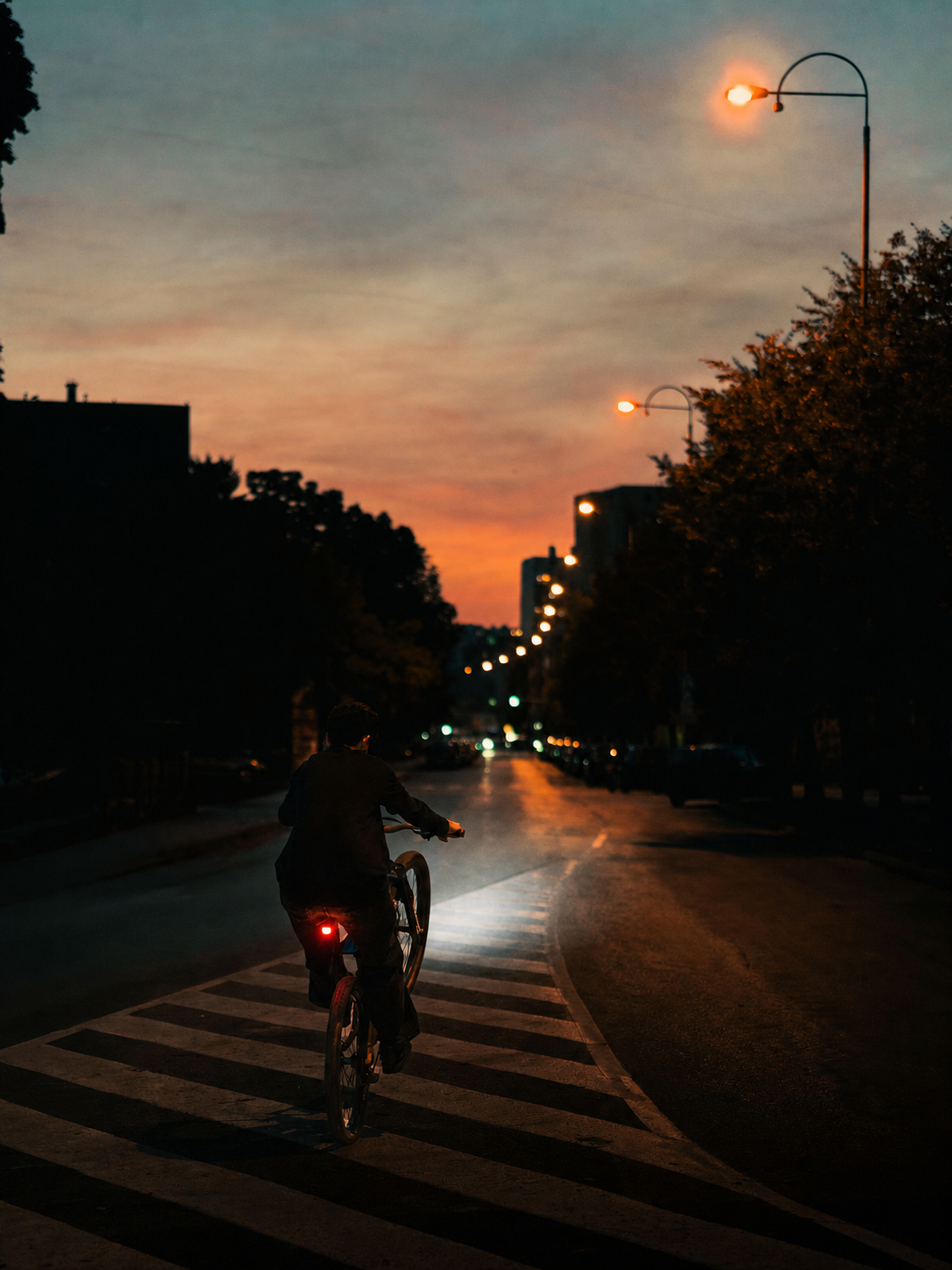 Cyclist using front and rear bike lights on a city street at dusk