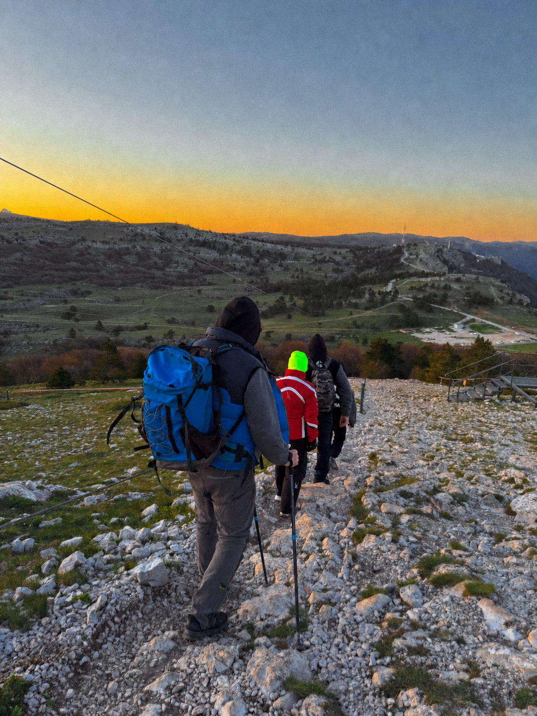 Hikers using trekking poles on a rocky mountain trail at sunset