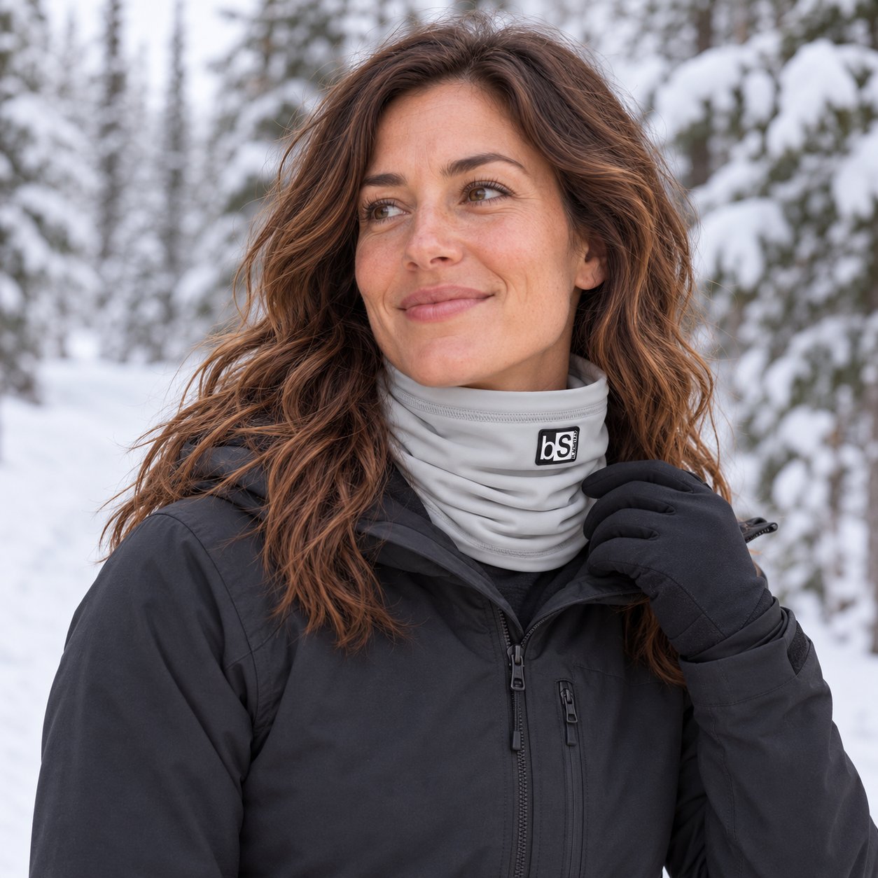 An adult wearing the Ash BlackStrap Dual Layer Tube around her neck during a pause on a snowy forest hiking trail.