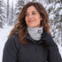 An adult wearing the Ash BlackStrap Dual Layer Tube around her neck during a pause on a snowy forest hiking trail.