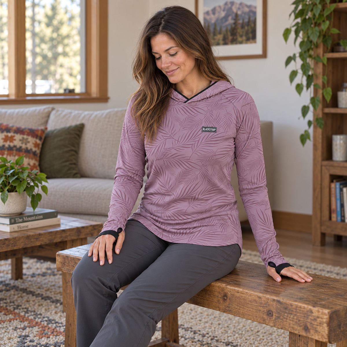 An adult seated at home wearing the BlackStrap Women's Brackish Sun Hoody in Ferns Mauve.