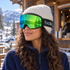 Woman wearing Green Emerald Bollé Nevada goggles over an off-white beanie outside a local coffee hut.