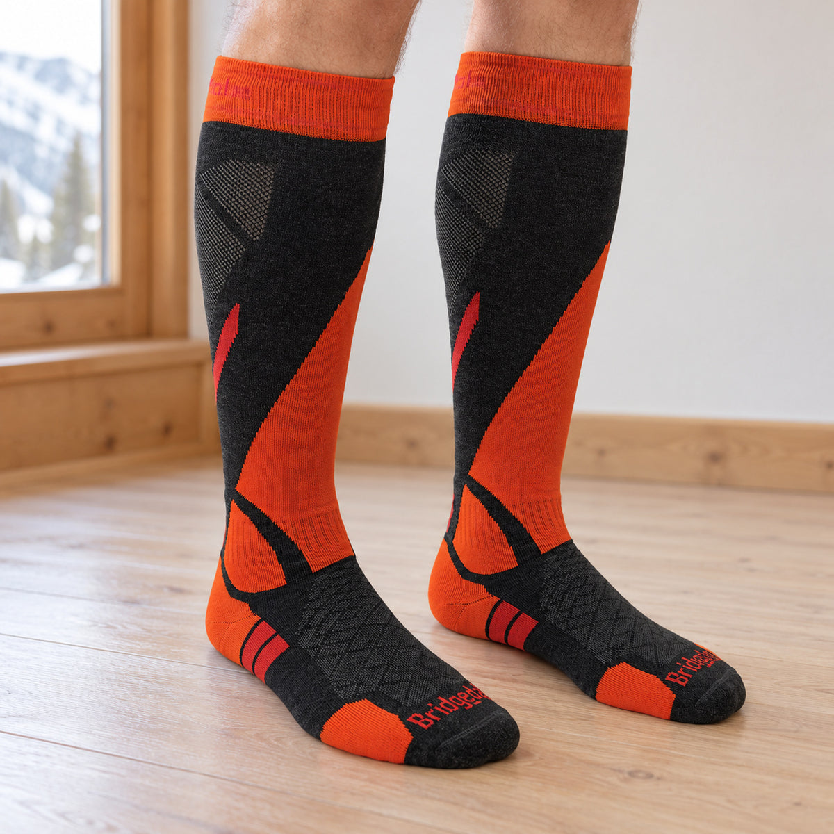 Grey and orange Bridgedale ski socks worn on two lower legs on a wooden floor.