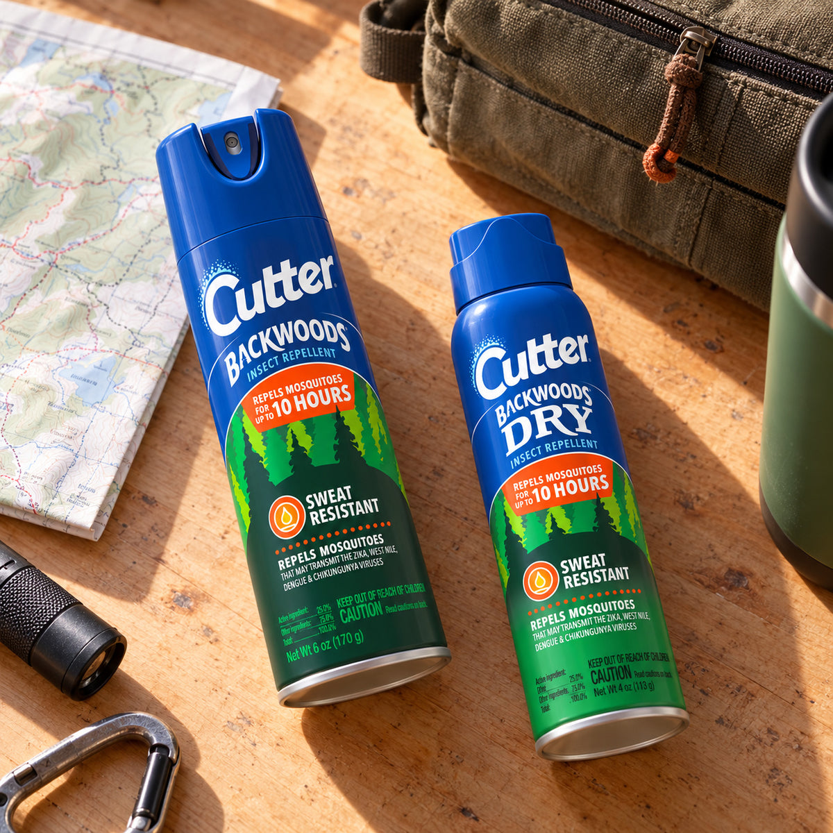 Cutter Backwoods 6 oz and Backwoods Dry 4 oz aerosol cans lying on a home workbench beside a map.