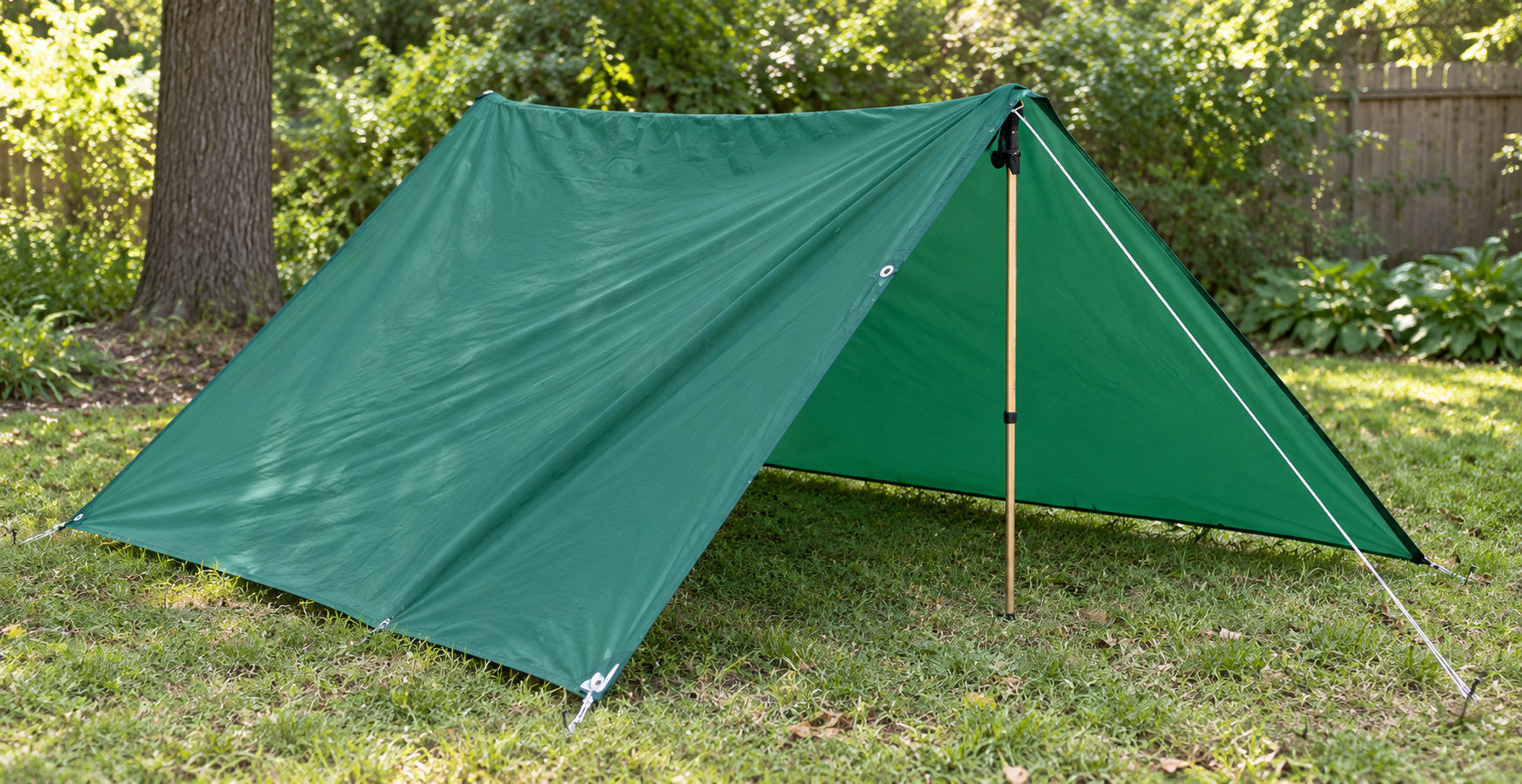 A green Equinox Egret nylon tarp in an open A-frame setup; support hardware shown for context.