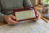 A compact burgundy Equinox Hellbender Ultralite Map Case Medium held in both hands above a map on a wooden planning workbench.