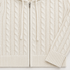 Close view of the cream cable-knit hoodie front showing the central zip, cream drawstrings, vertical cable pattern, ribbed hem and ribbed cuff.