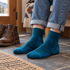 Person wearing deep teal blue socks with cuffed jeans beside boots in a home entryway.