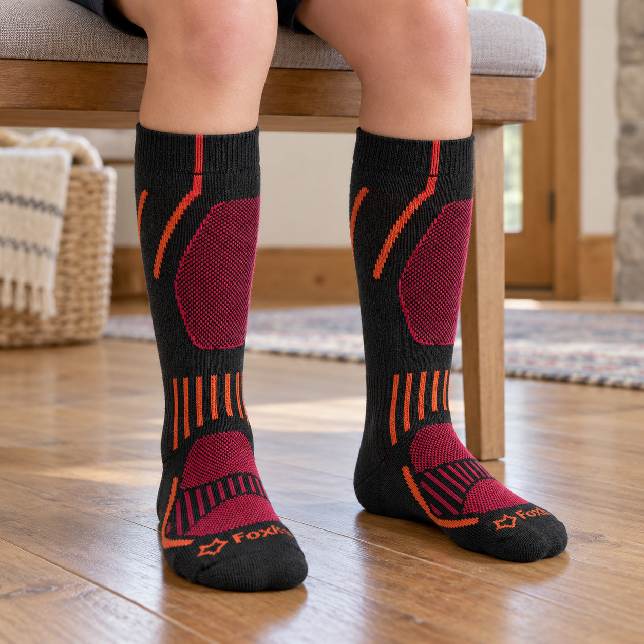 Black Fox River Boreal kids ski socks with orange and magenta details, worn while seated.