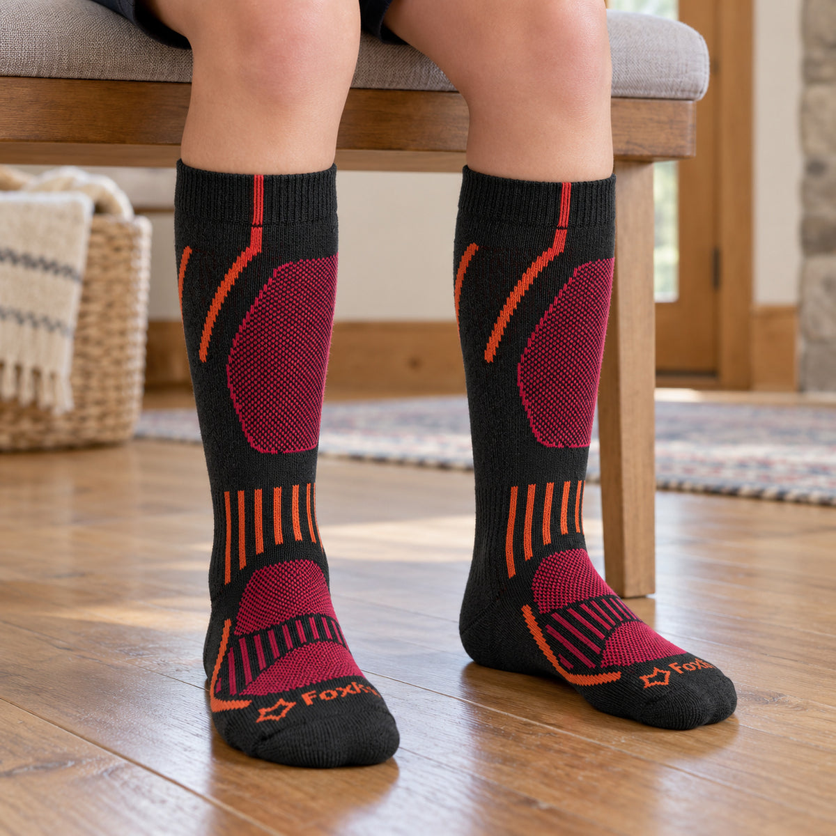 Black Fox River Boreal kids ski socks with orange and magenta details, worn while seated.