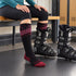 Women's Summit ski socks during ski preparation, with one foot in a black alpine ski boot and the other sock fully visible.