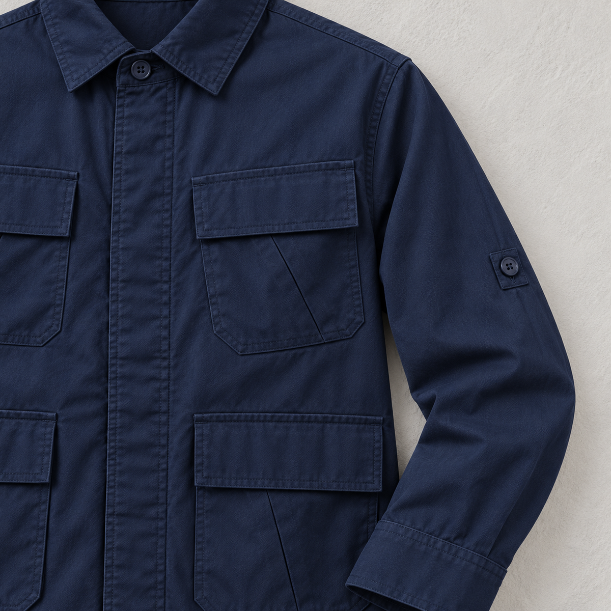 Close view of navy jacket plain pocket flaps, covered placket, cuff, and woven fabric.