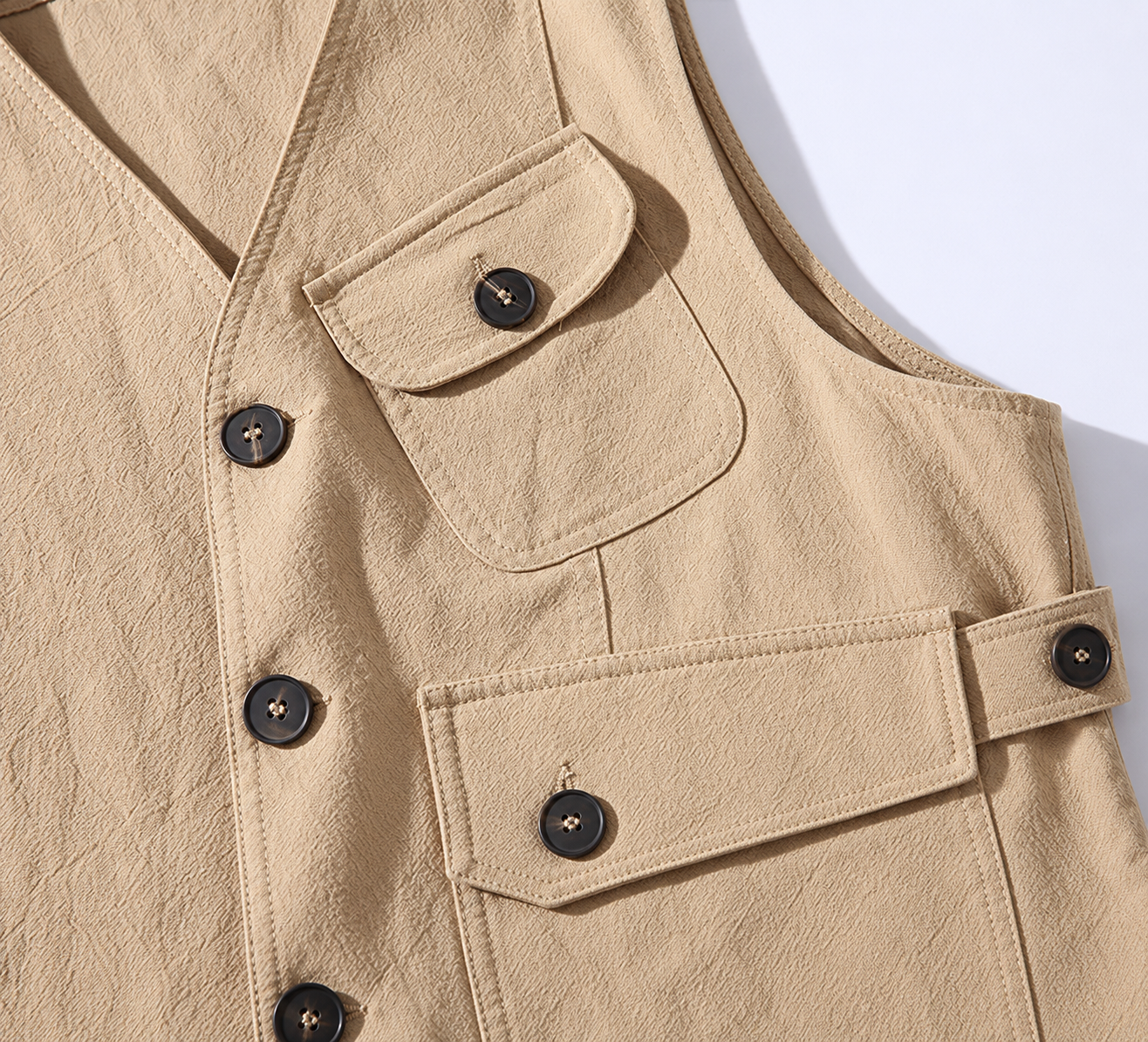 Close view of khaki vest flap pockets, dark buttons, and side adjustment tab.