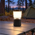 Black LUXPRO LP189 mini lantern lighting a folding camping table beside a tent at dusk