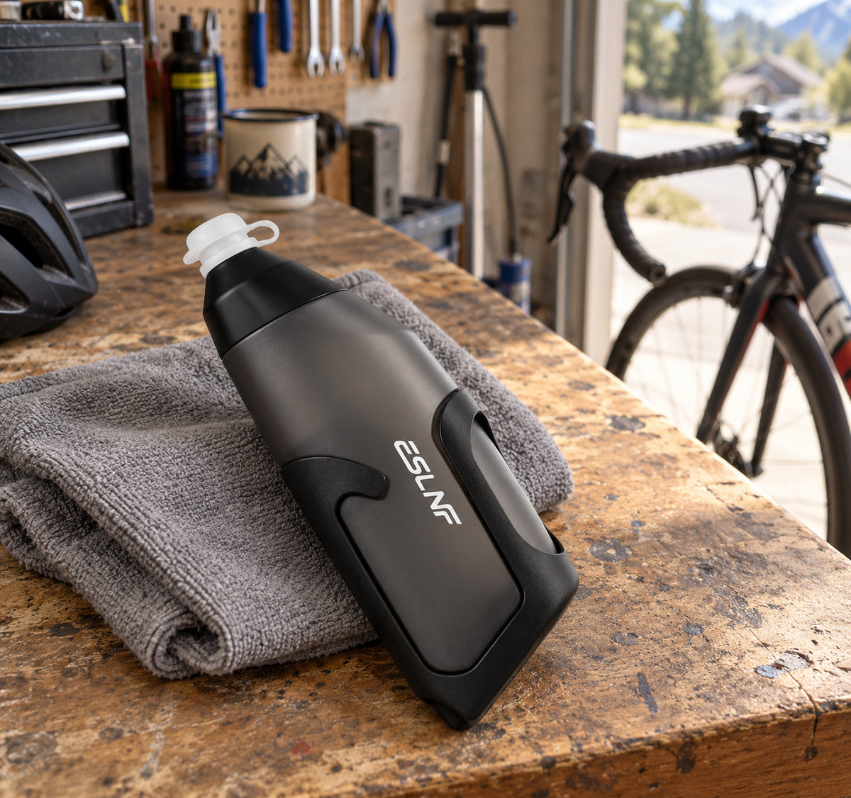Charcoal cycling bottle and matching holder resting on a towel on a home garage workbench