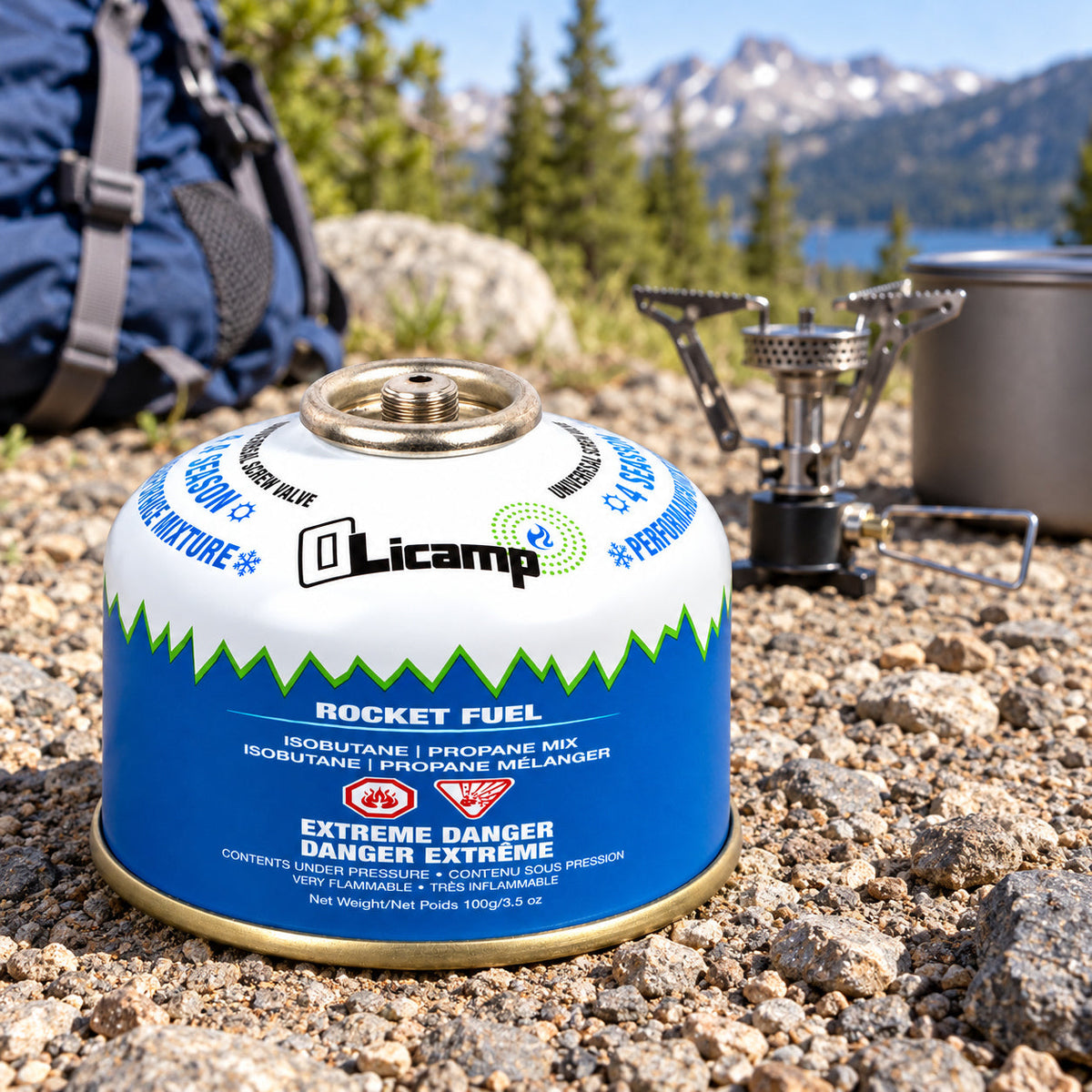 An Olicamp Rocket Fuel 100 g canister beside separate unlit cooking equipment at an outdoor campsite.