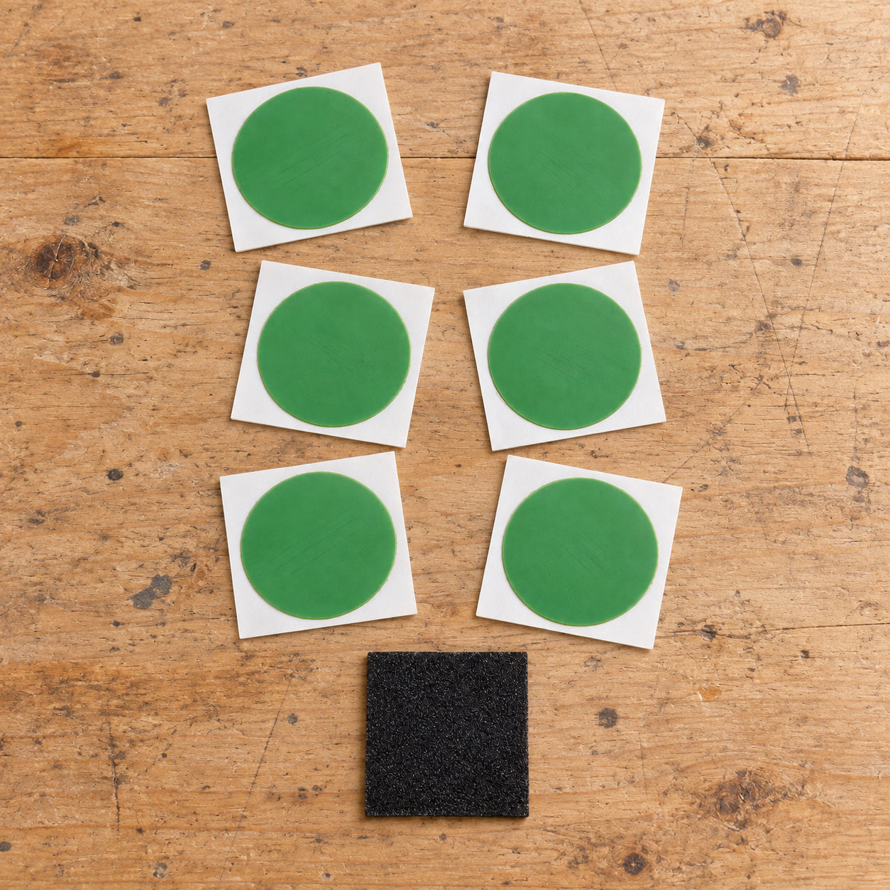 Six Planet Bike patch cards and the abrading square arranged on a wooden repair bench