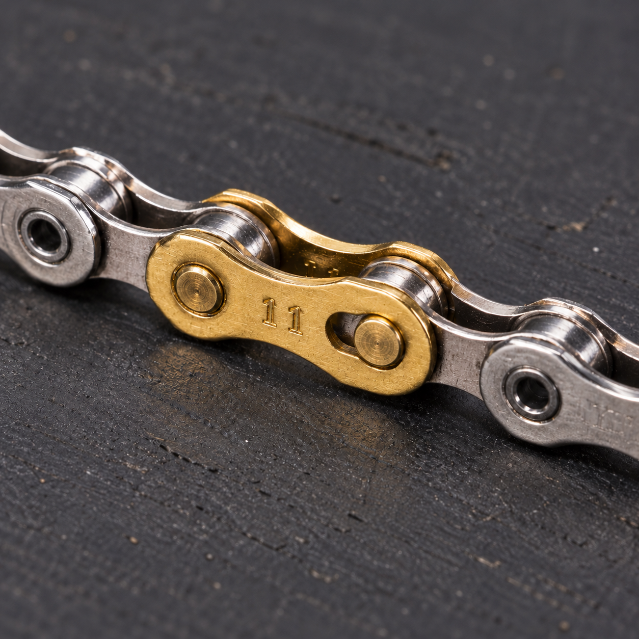 Gold YBN QRs11 11-speed quick link joining a silver bicycle chain on a dark repair mat
