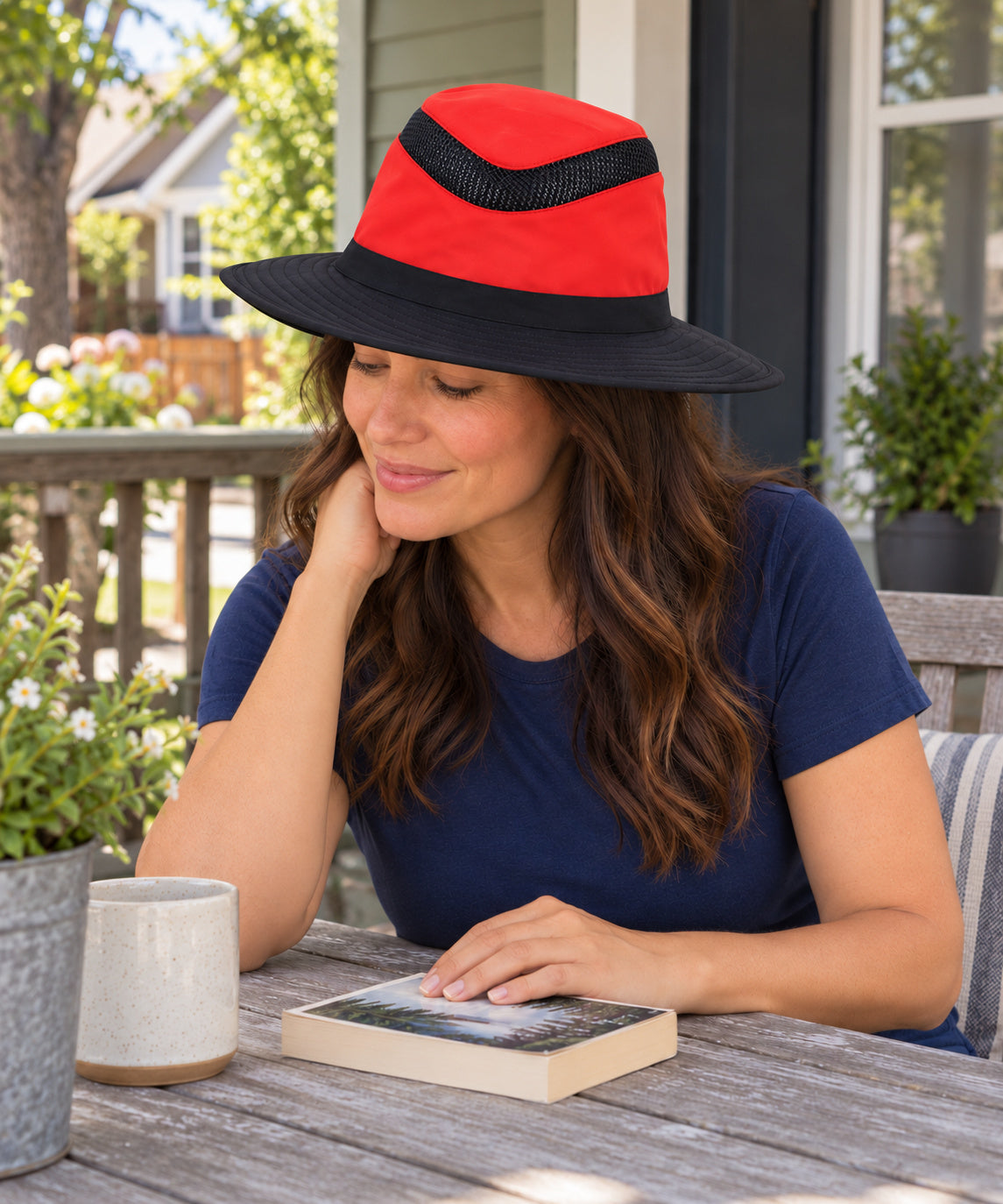 A woman wearing a red and black Tilley LTM6 Airflo hat while seated on a porch, with one hand resting on a closed book.