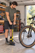 A cyclist using a yellow Topeak JoeBlow Sport III floor pump beside a bicycle in a home garage.