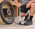 Silver Topeak Mountain Morph inflating an explicitly detached bicycle wheel, with one hose and a foot-stabilized base.