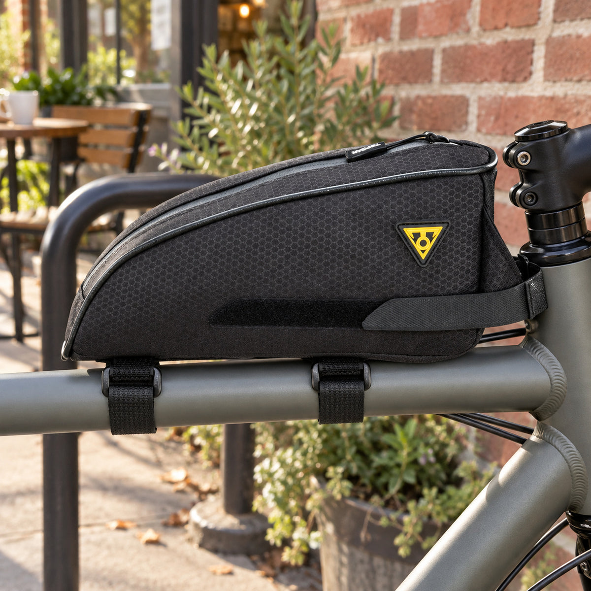 Black Topeak TopLoader bag mounted on a bicycle top tube outside a neighborhood cafe
