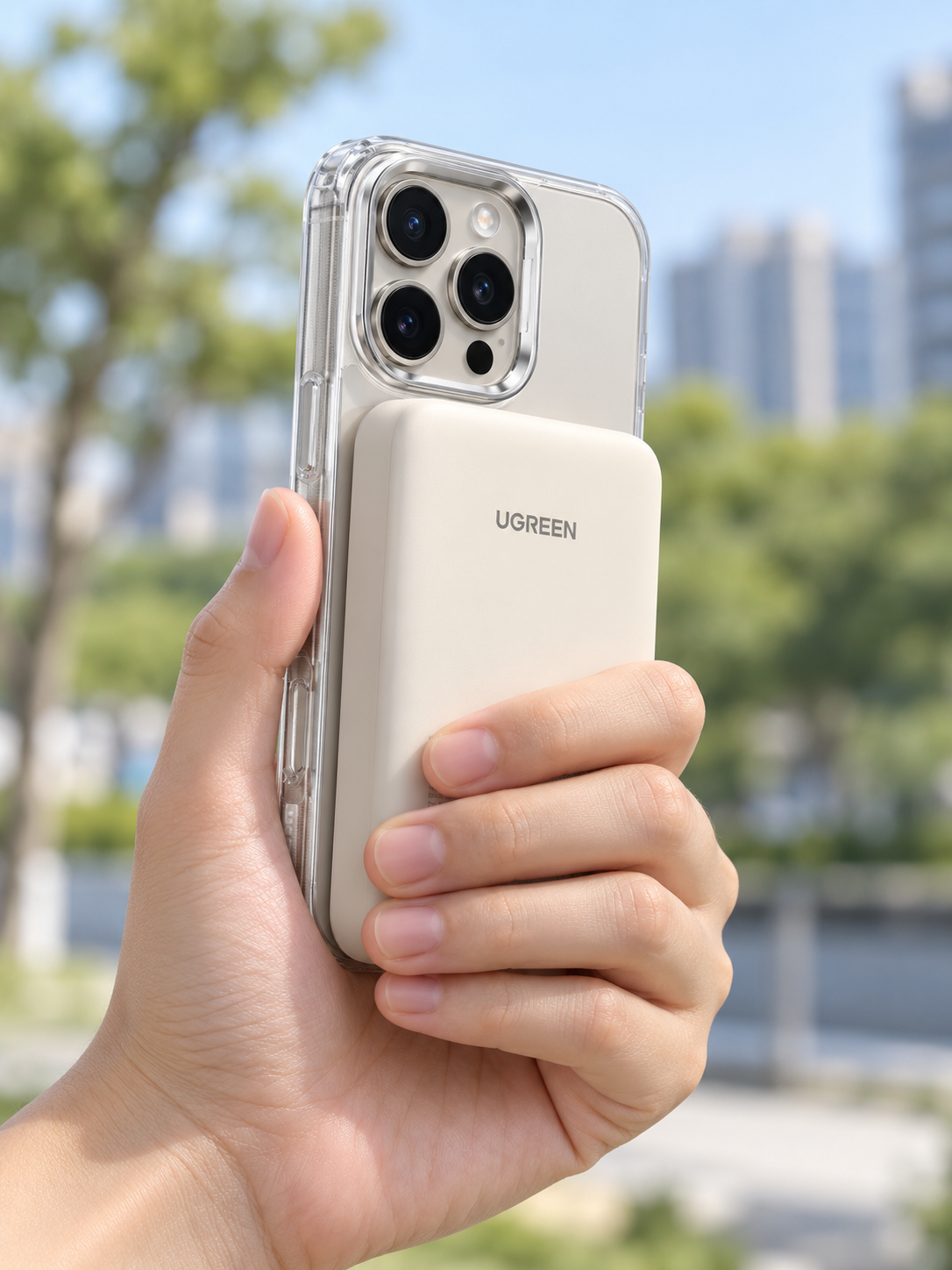 White UGREEN PB561 power bank seated against the back of a phone in a clear magnetic case, held in one hand with camera clearance and bank thickness visible; phone and case are demonstration props, not included.