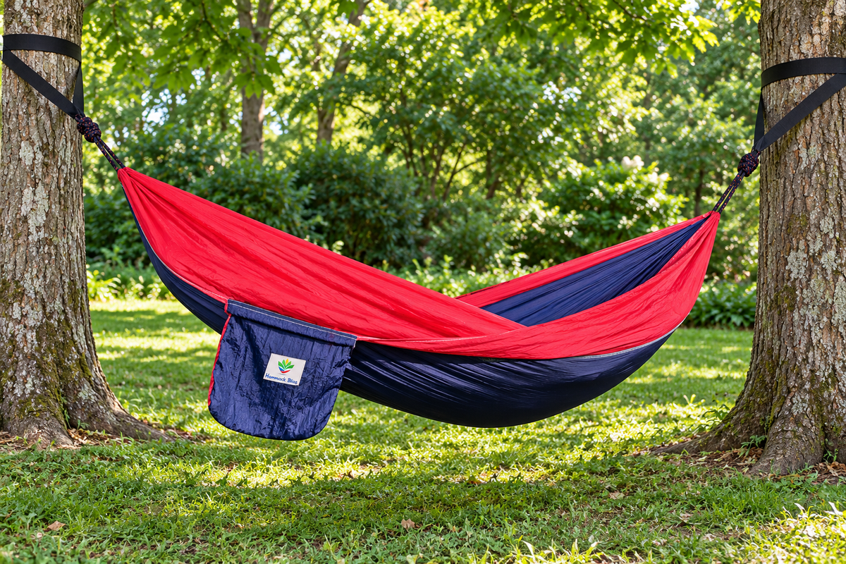 Empty Navy/Red Hammock Bliss Single suspended low between two trees, with both rope connections visible on separate black tree straps; tree straps are not included.